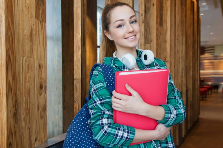Smiling student holding book and wearing headphones, ready for study. college fashion