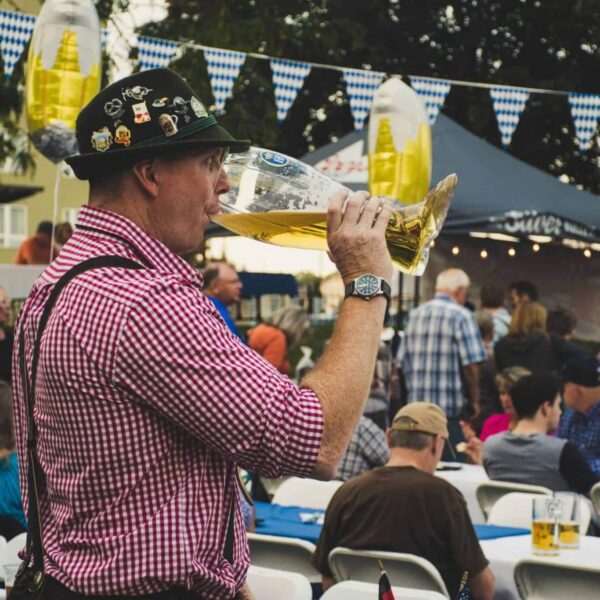 Oktoberfest, West Central Florida, Man enjoying a large beer mug at an Oktoberfest celebration outdoors with a lively crowd.