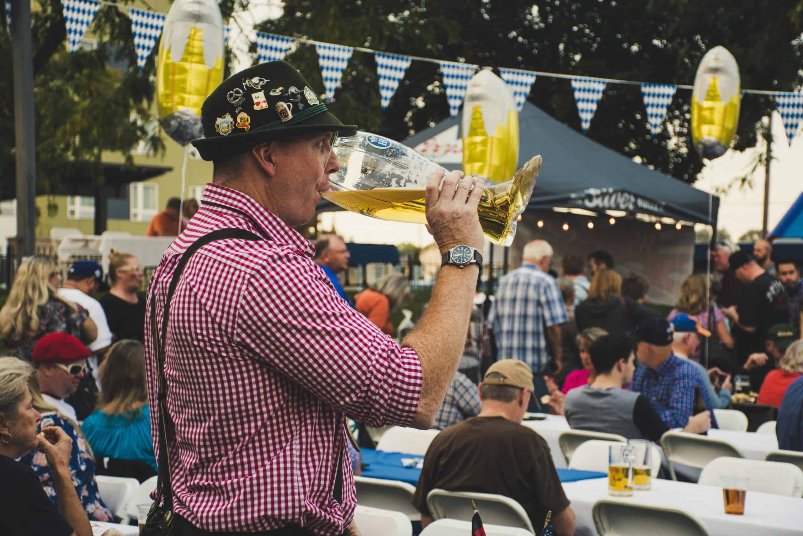 Oktoberfest, West Central Florida, Man enjoying a large beer mug at an Oktoberfest celebration outdoors with a lively crowd.