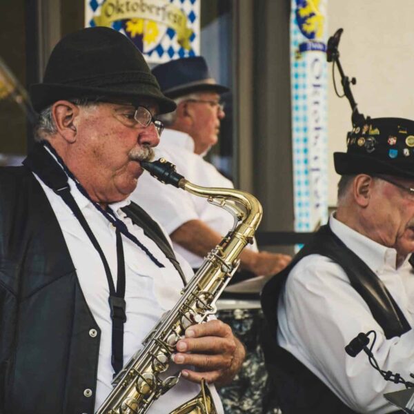 Elderly musicians perform with saxophone and trumpet at an Oktoberfest festival outdoors.