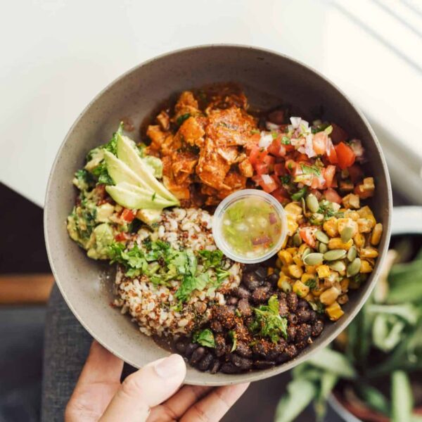 Top view of a vibrant vegan Buddha bowl with quinoa, avocado, and fresh salsa in hand.