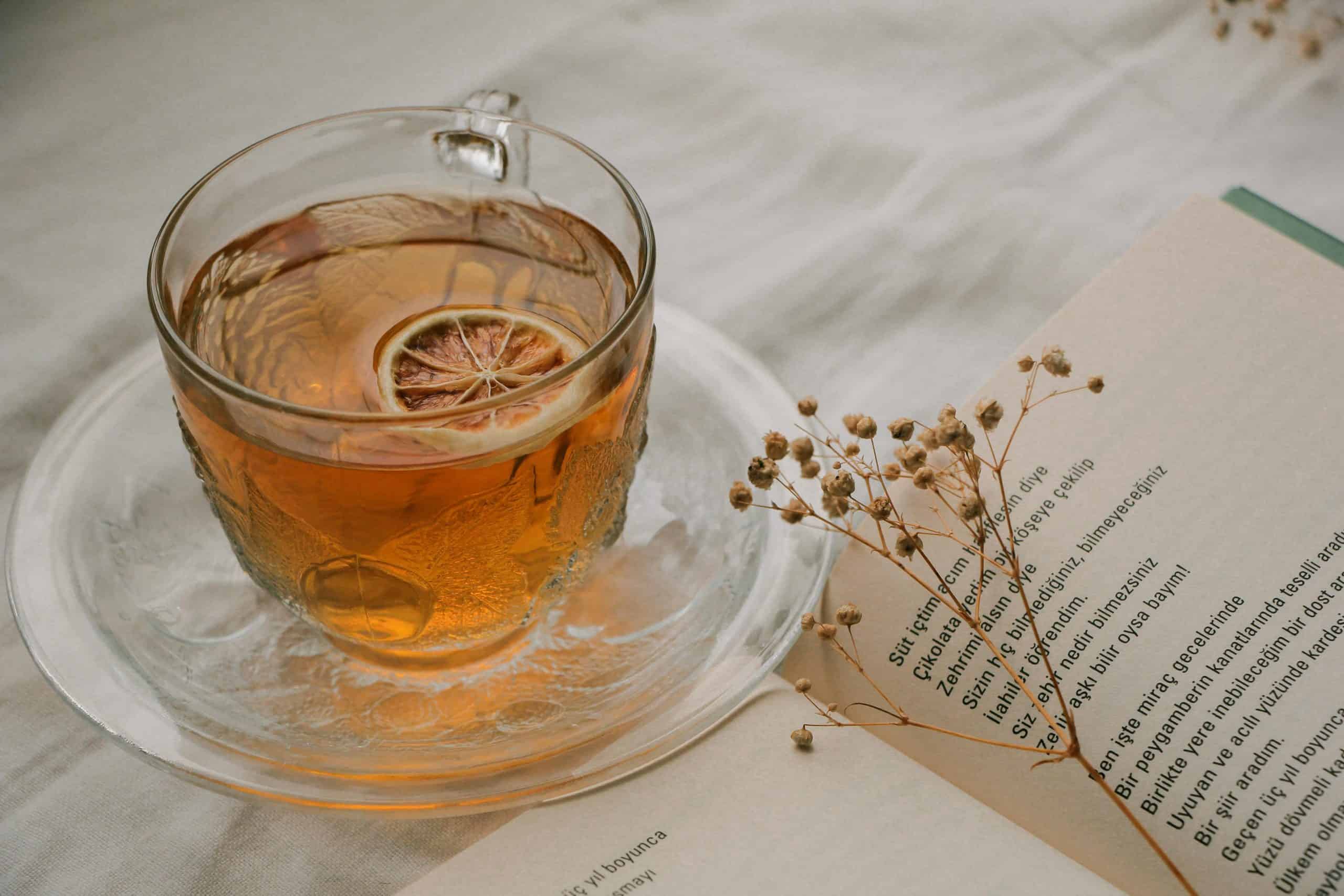A warm cup of tea with a dried slice of lemon next to an open book and delicate floral accent, perfect for relaxation.