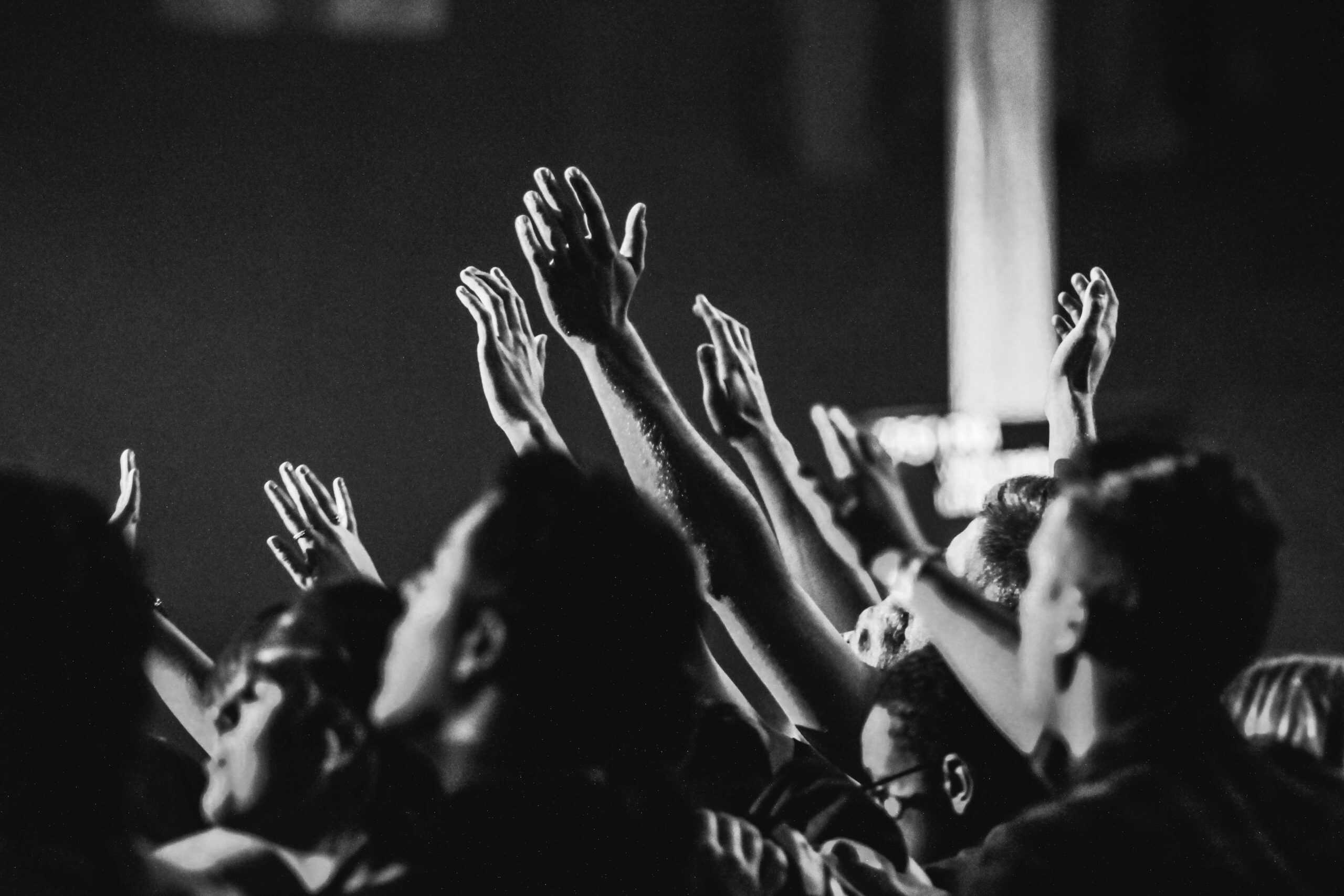 Dynamic black and white photo of a concert audience with hands raised, capturing, the energy of live music, daily devotion