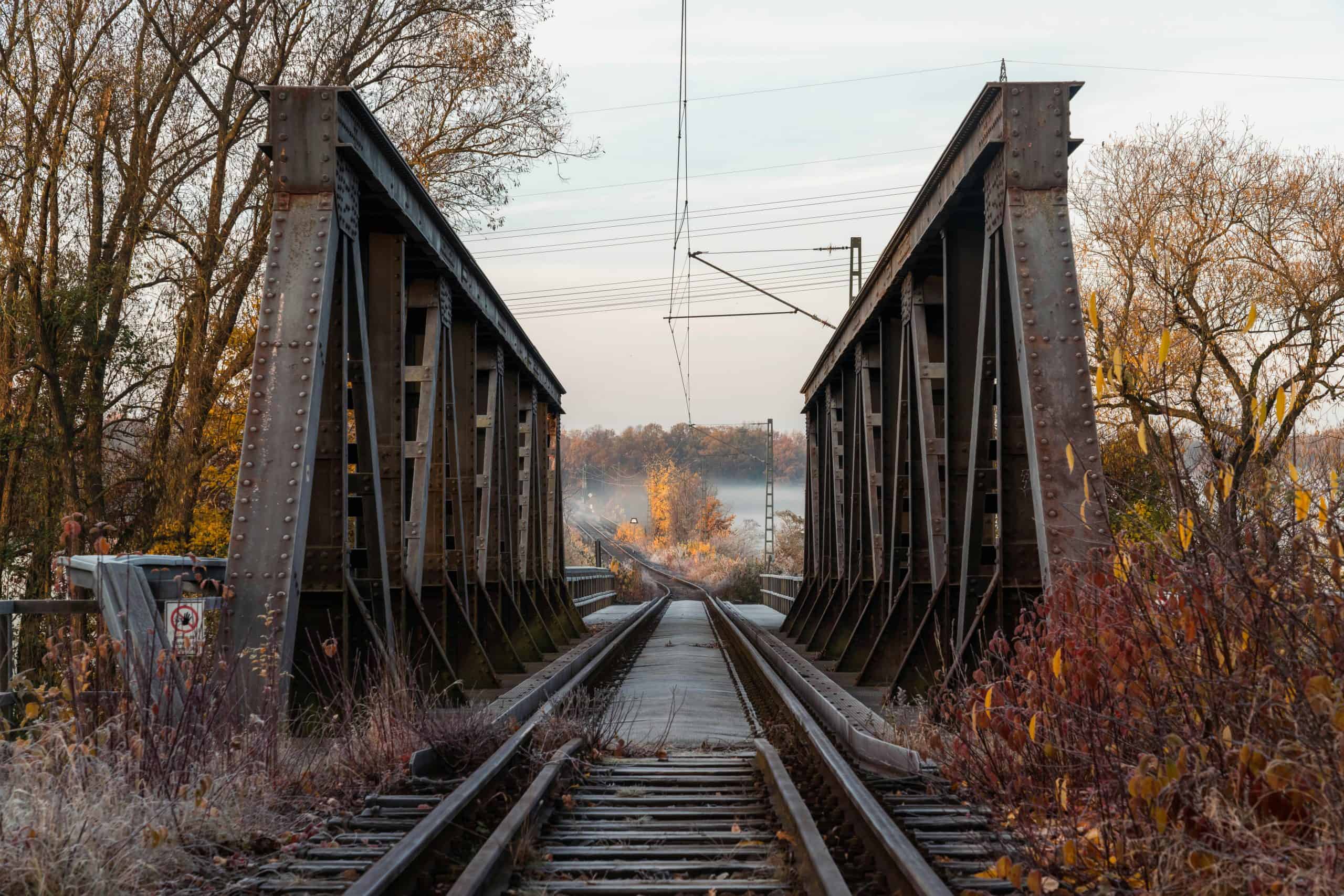 Steel railway bridge in autumn with fog and fall foliage during sunrise.