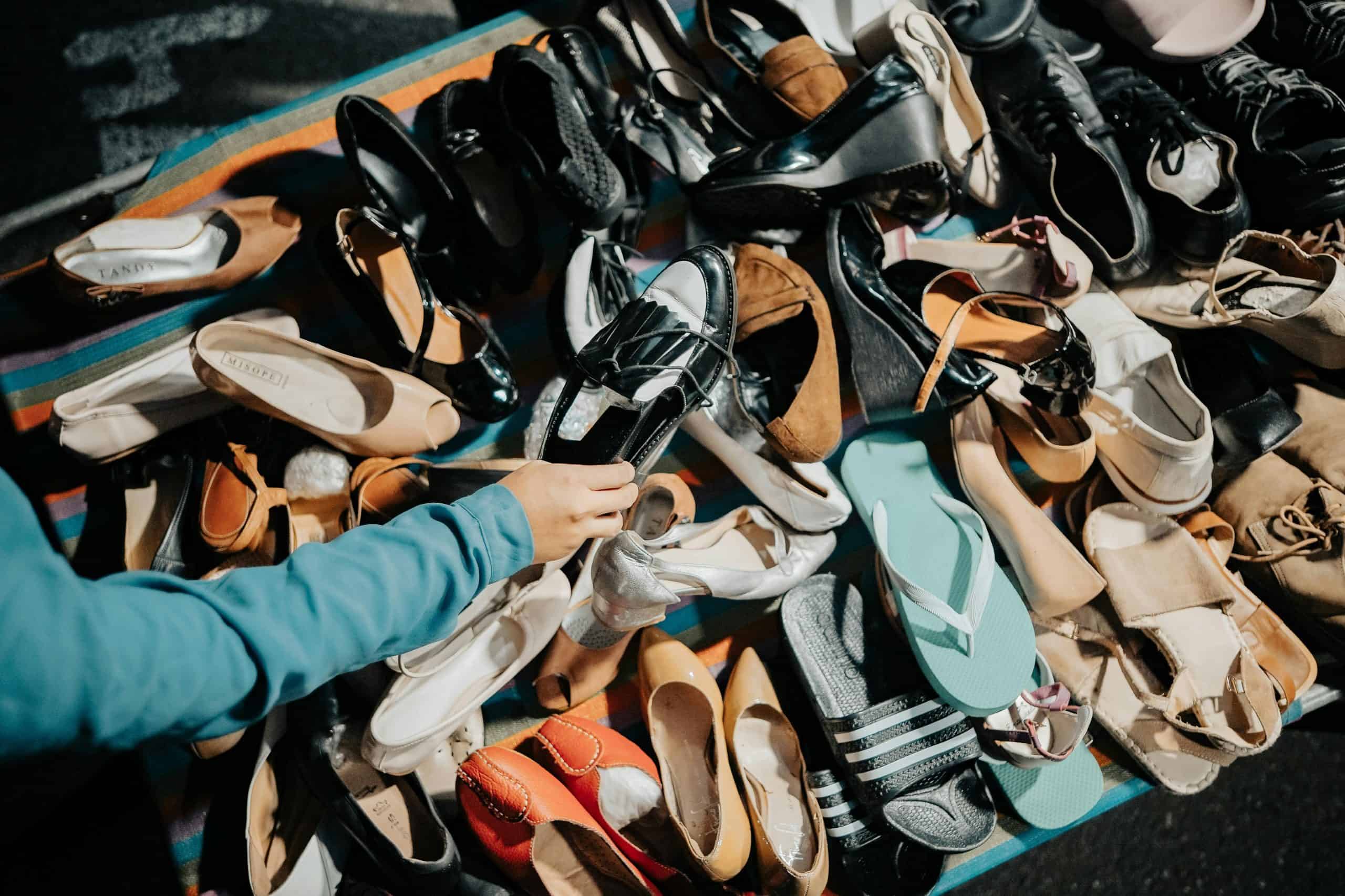 A variety of footwear displayed at an outdoor market stall with a hand selecting a shoe.