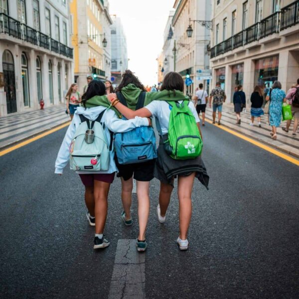 Three young friends walk arm-in-arm on a Lisbon street, showcasing friendship and travel spirit.