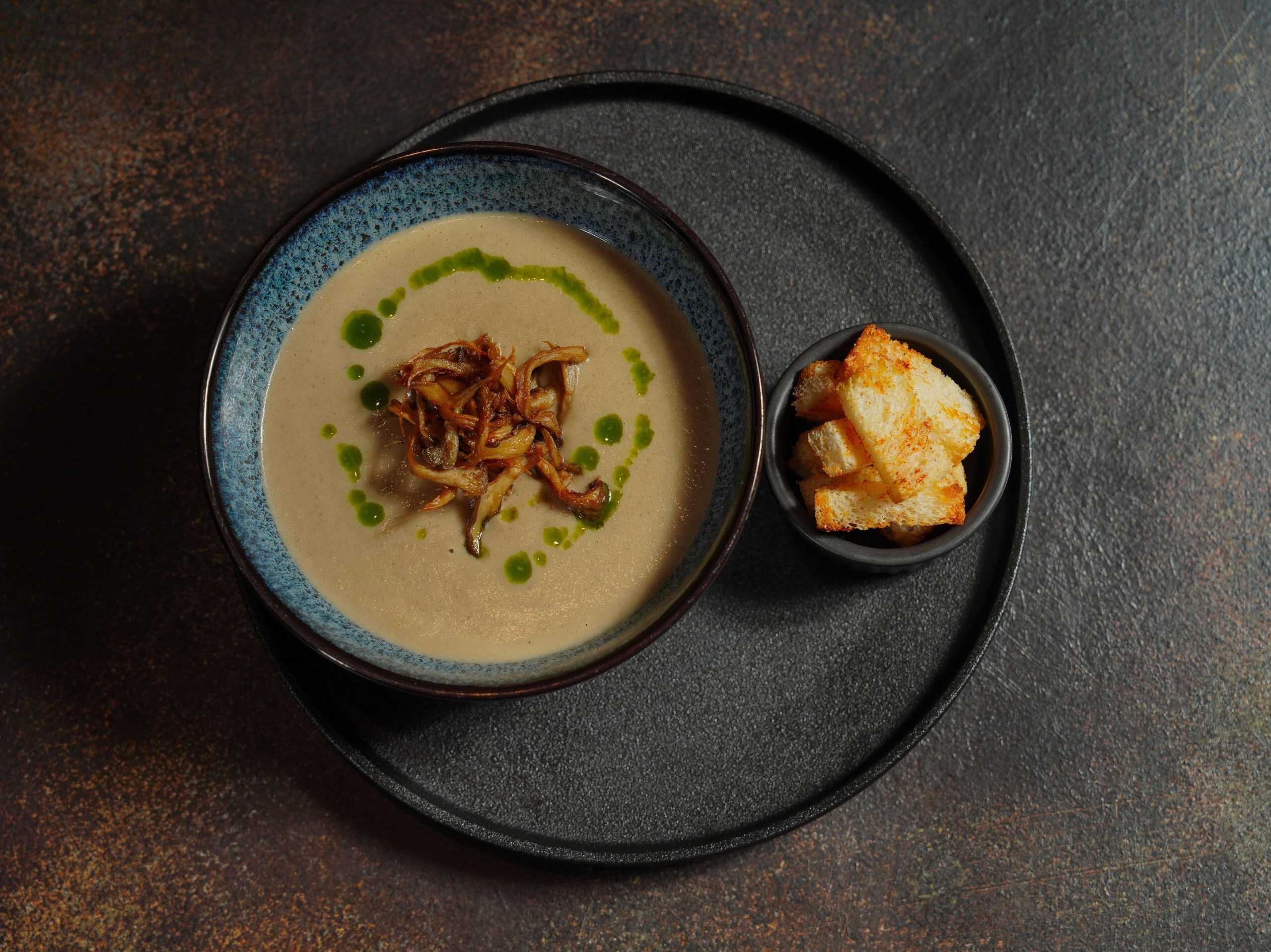 Delicious creamy mushroom soup with crispy croutons, elegantly presented on a stone background.