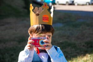 burger king, halloween toy, Young boy with Burger King crown using paper camera outside on a sunny day.
