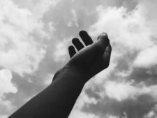 A monochrome image of a hand reaching toward the cloudy sky, symbolizing aspiration. daily devotion