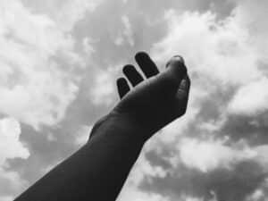 A monochrome image of a hand reaching toward the cloudy sky, symbolizing aspiration. daily devotion