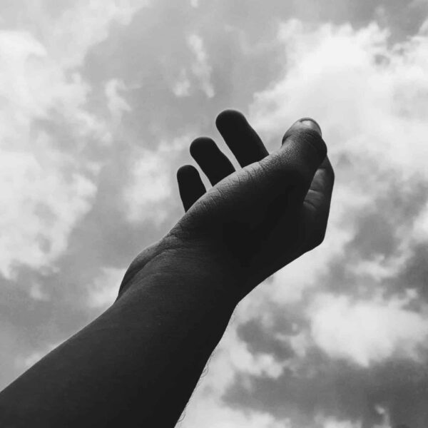 A monochrome image of a hand reaching toward the cloudy sky, symbolizing aspiration. daily devotion