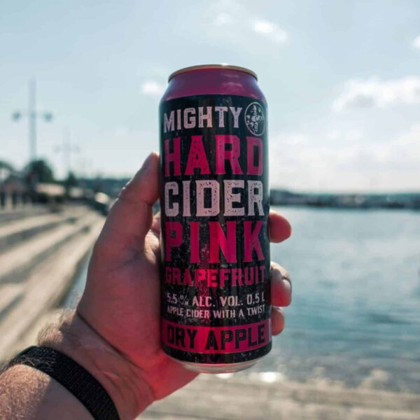 Person holding a grapefruit hard cider can near a scenic waterfront in Lahti, Finland, enjoying a refreshing fall drink outdoors.