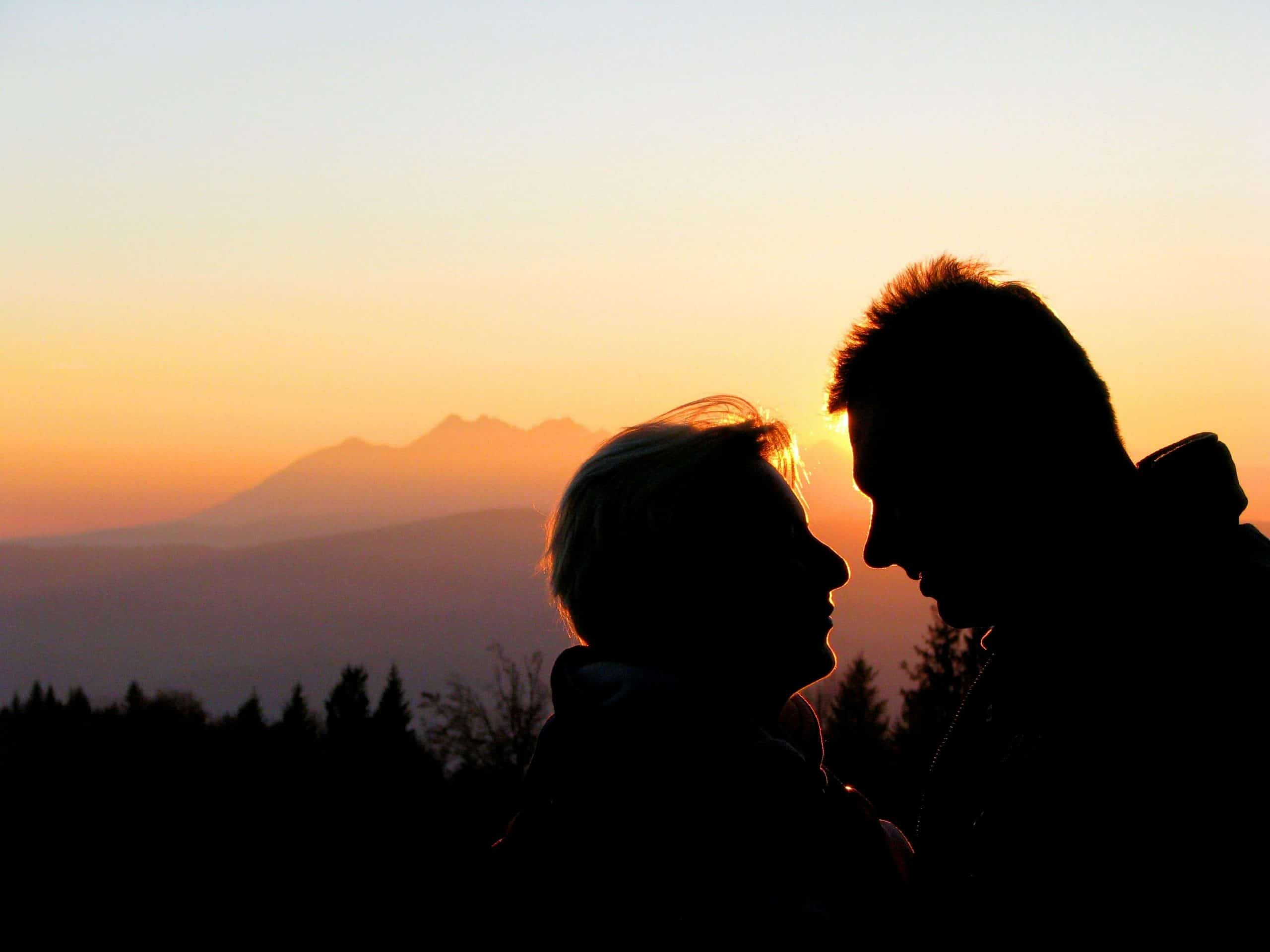 Silhouette of a couple sharing a tender moment against a mountain sunset.