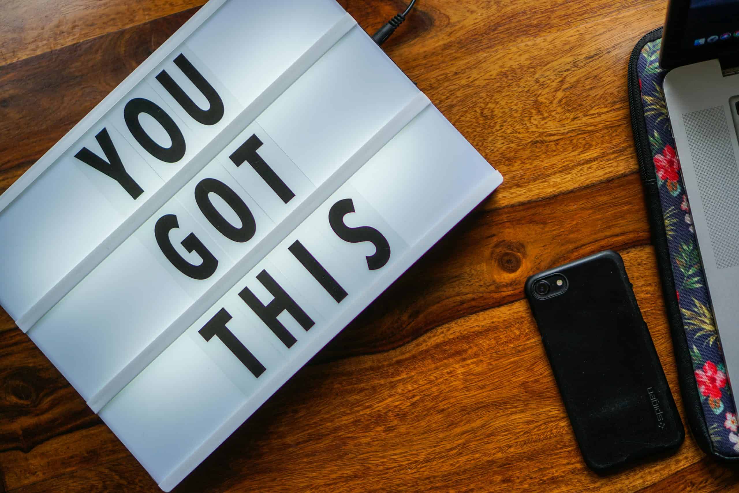 Motivational quote 'You Got This' on a lightbox, smartphone on a wooden table, cozy workspace vibe.