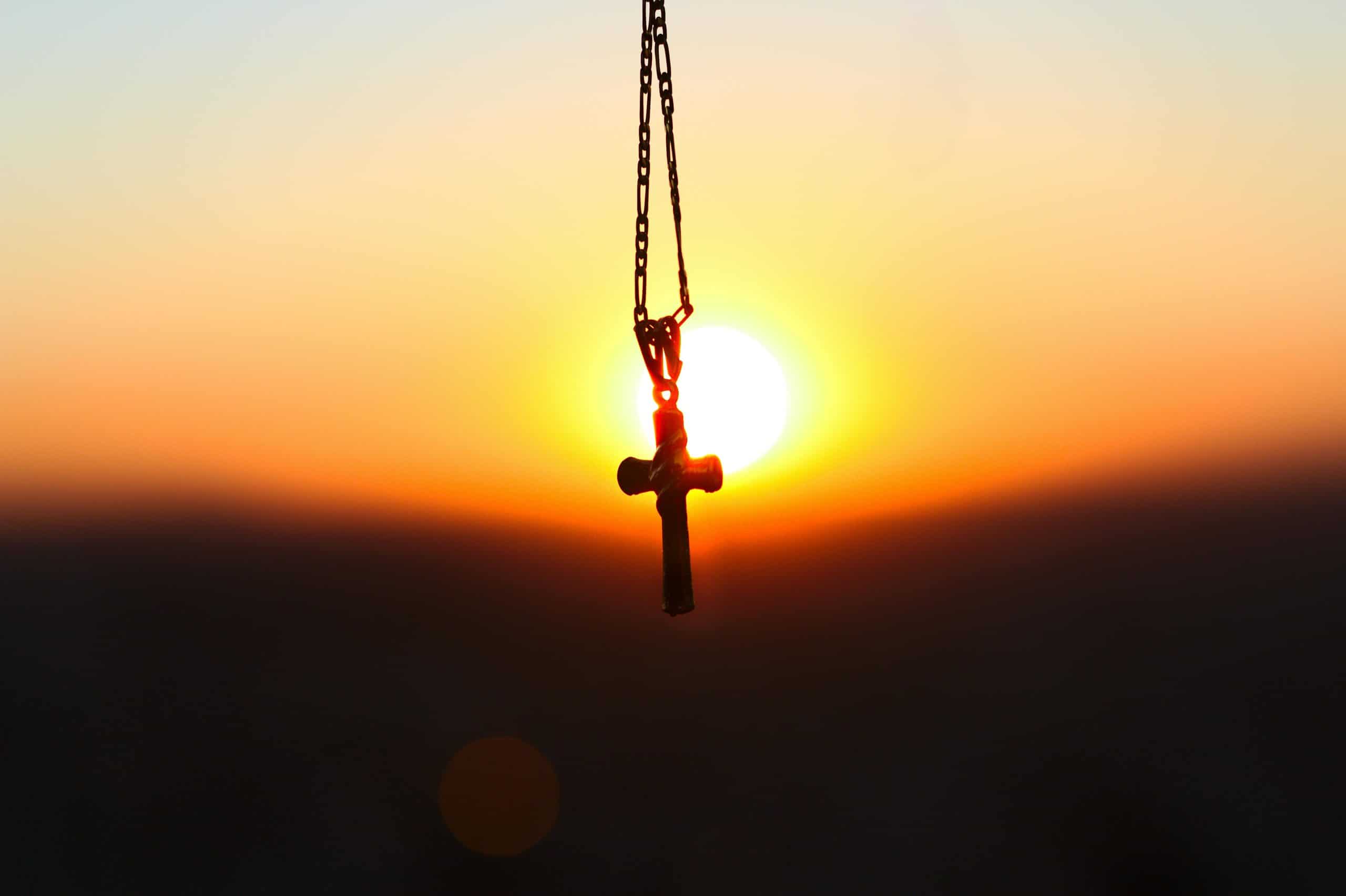 A cross pendant silhouetted against a vibrant sunset, symbolizing faith and peace, daily devotion