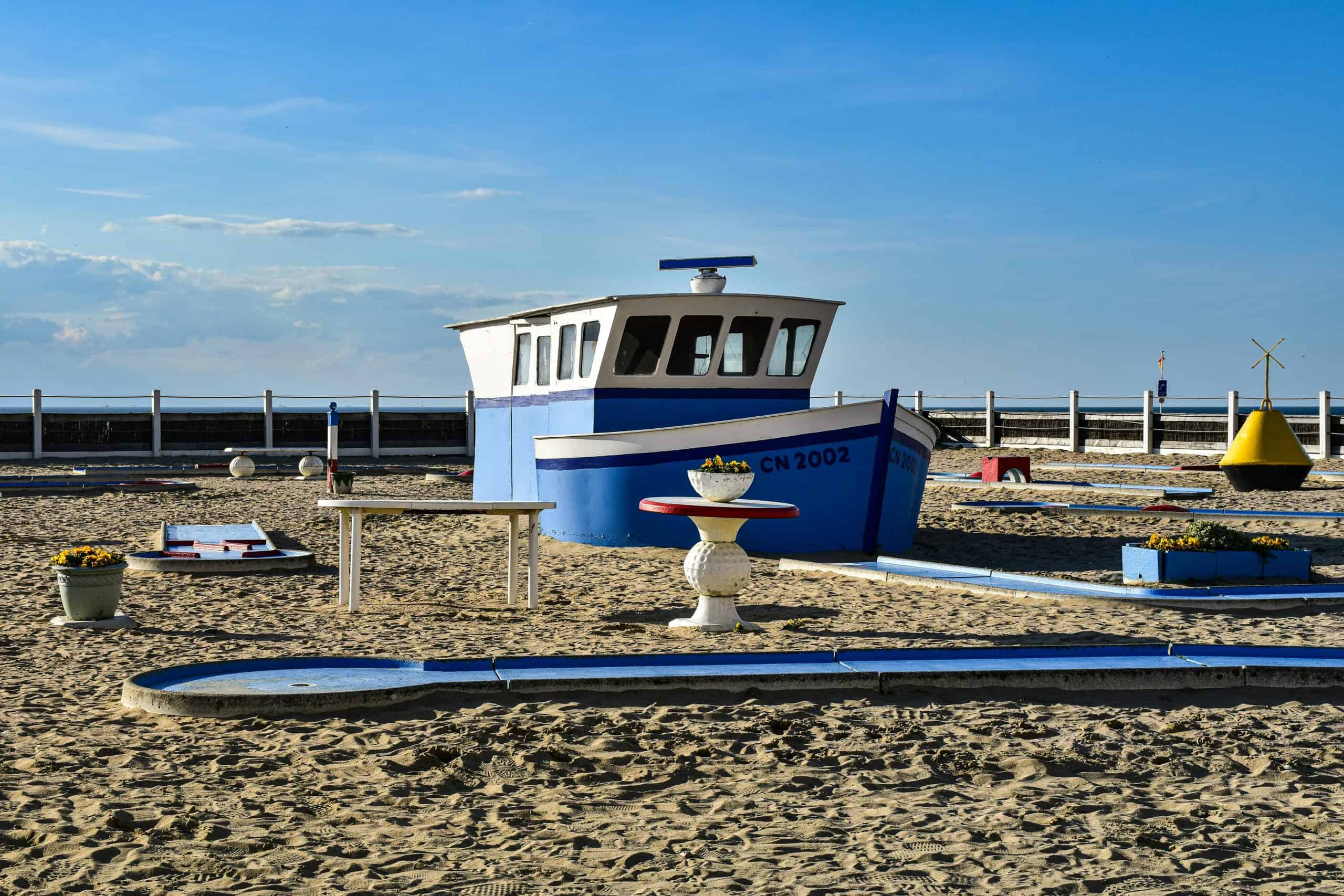 Quirky mini-golf course on a beach with a blue and white boat feature, under a clear sky.