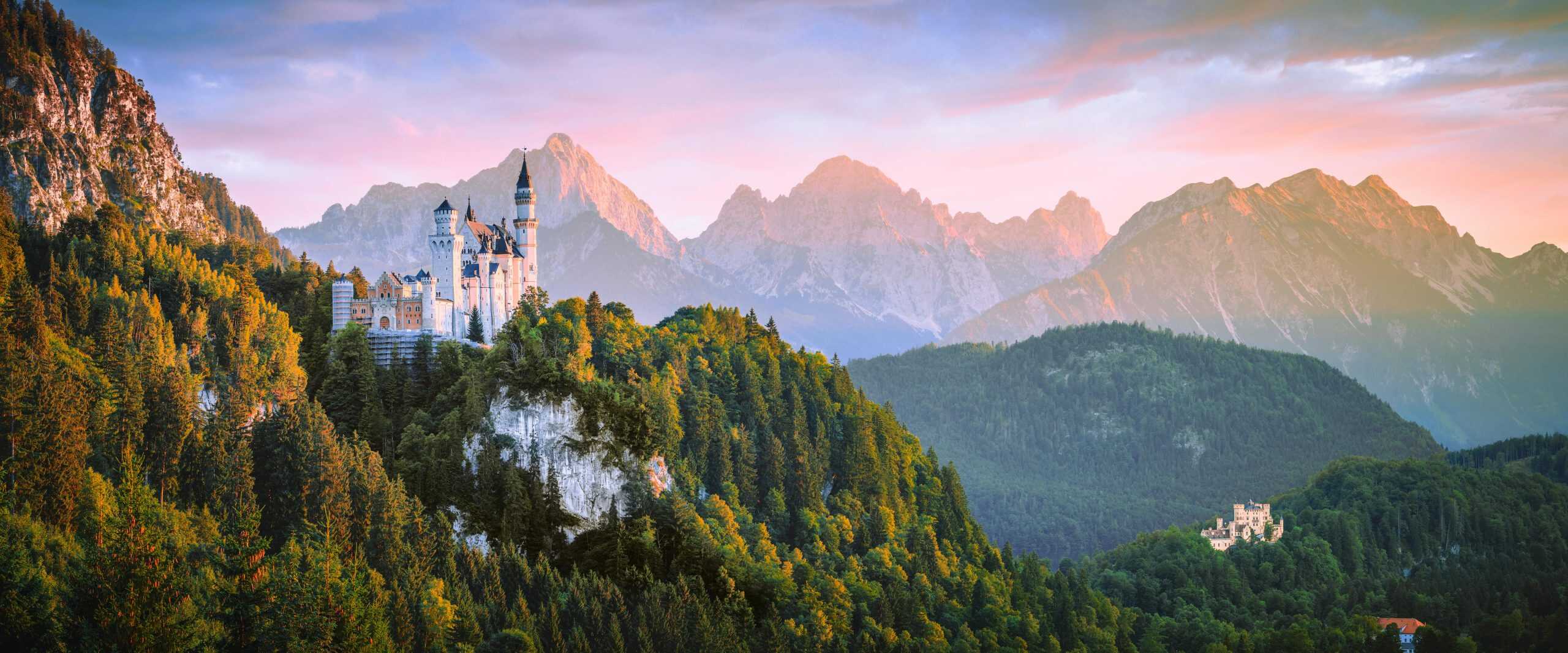 Breathtaking view of Neuschwanstein Castle with Alps in the background during sunset.