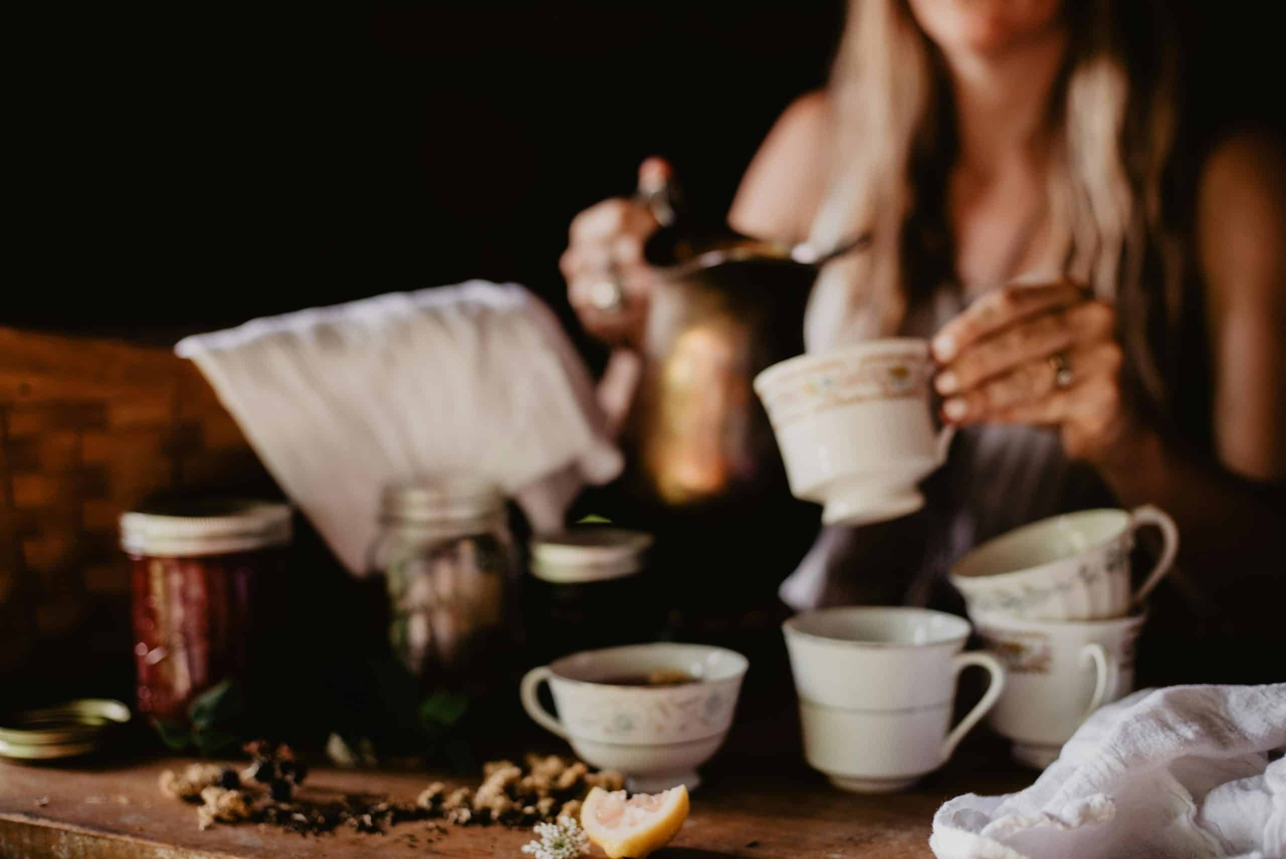 Warm indoor tea setting with porcelain cups, jam jars, and a woman serving tea for relaxation.
