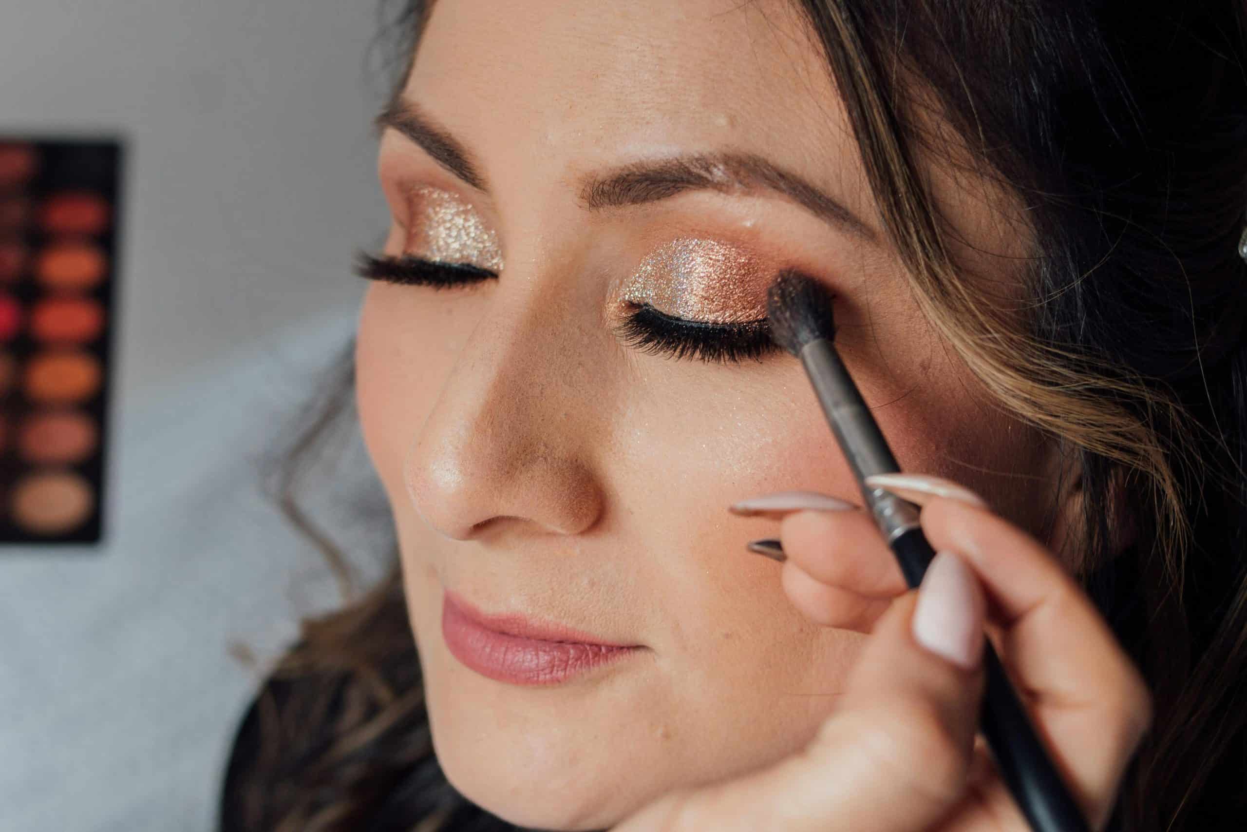 Woman receiving glamorous makeup with glitter eyeshadow and long lashes.