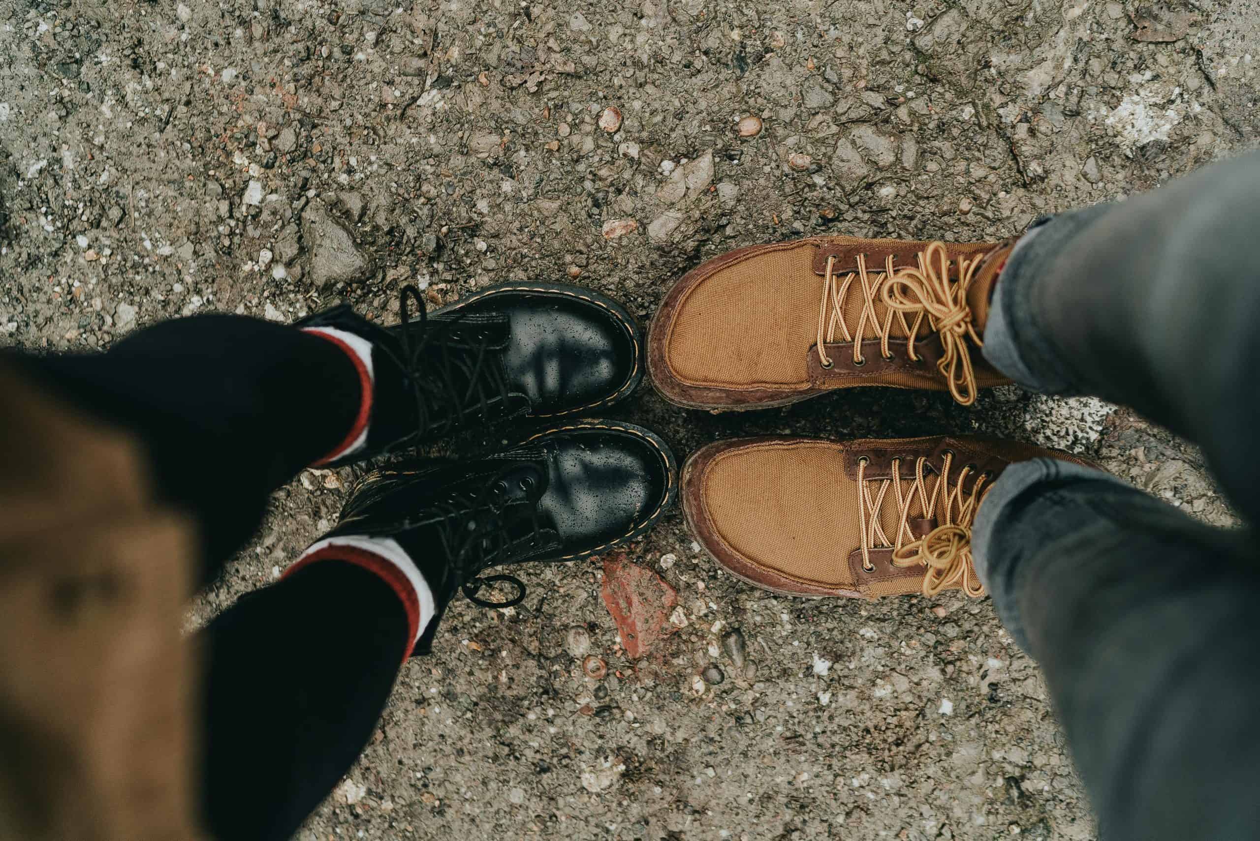 Two pairs of stylish boots on rough ground, showcasing fashion footwear contrast.