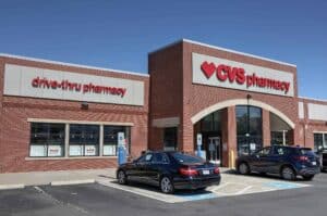 CVS Pharmacy storefront with drive-thru and parked cars, illustrating the CVS recall involving baby drops, colon cleanser, and ice cream products.