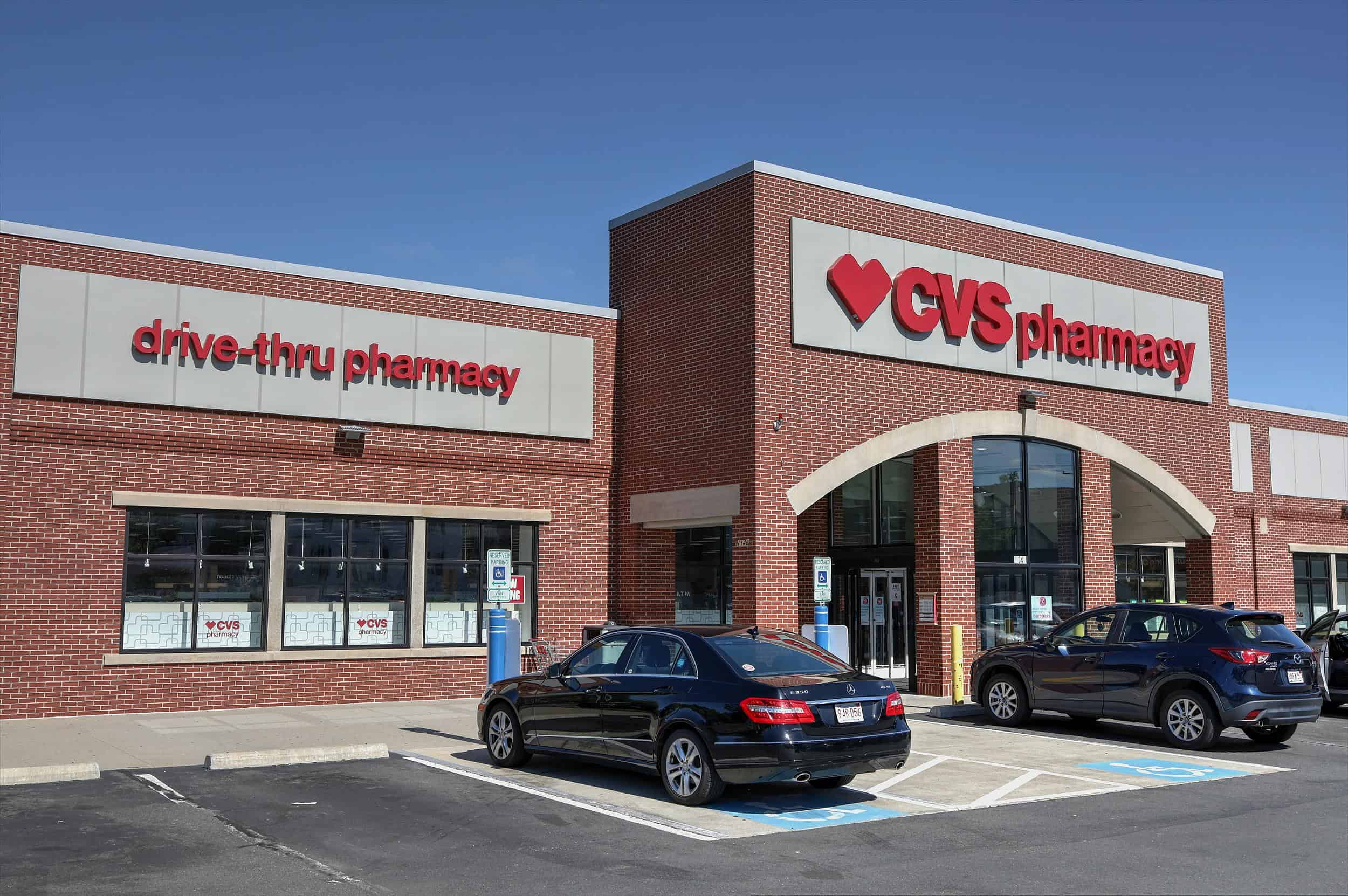 CVS Pharmacy storefront with drive-thru and parked cars, illustrating the CVS recall involving baby drops, colon cleanser, and ice cream products.