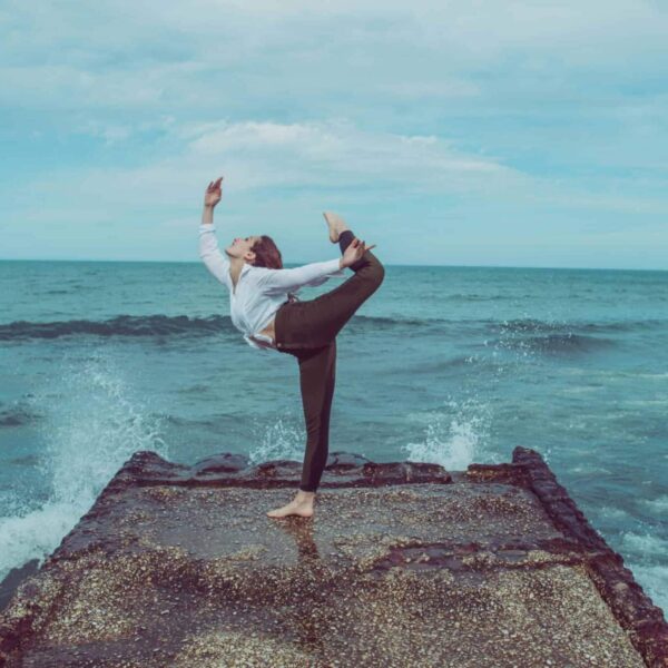 A person practices a high-level yoga pose on a pier by the ocean, capturing serene balance.