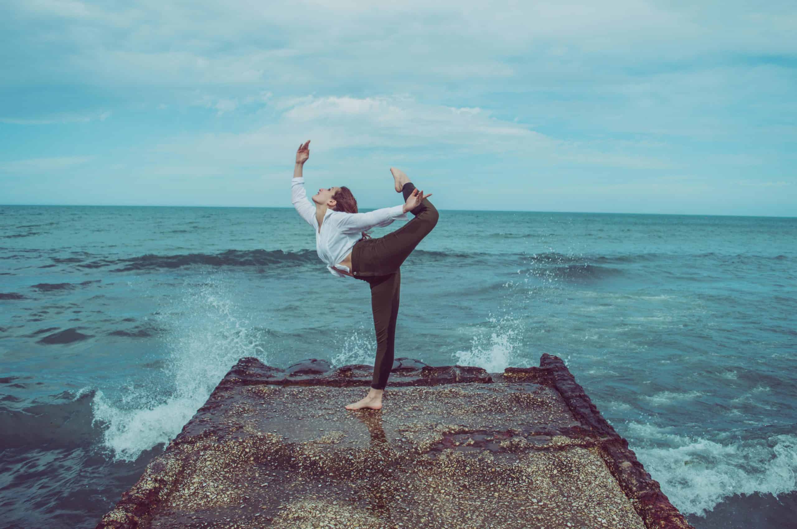 A person practices a high-level yoga pose on a pier by the ocean, capturing serene balance.