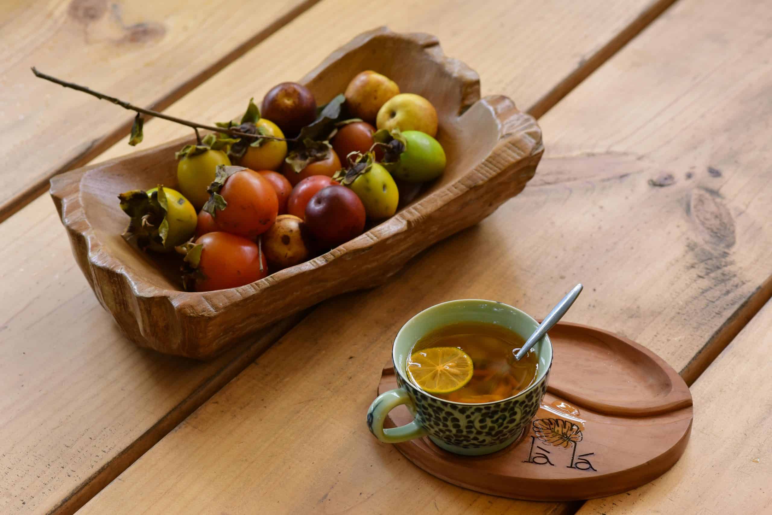 Apple cider, A cozy setup with a wooden bowl of fruits and a cup of herbal tea on a wooden table.