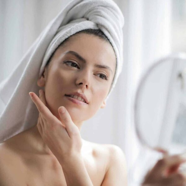 This photograph features a woman at home looking in a mirror. A home facial steamer can be part of a skincare routine.