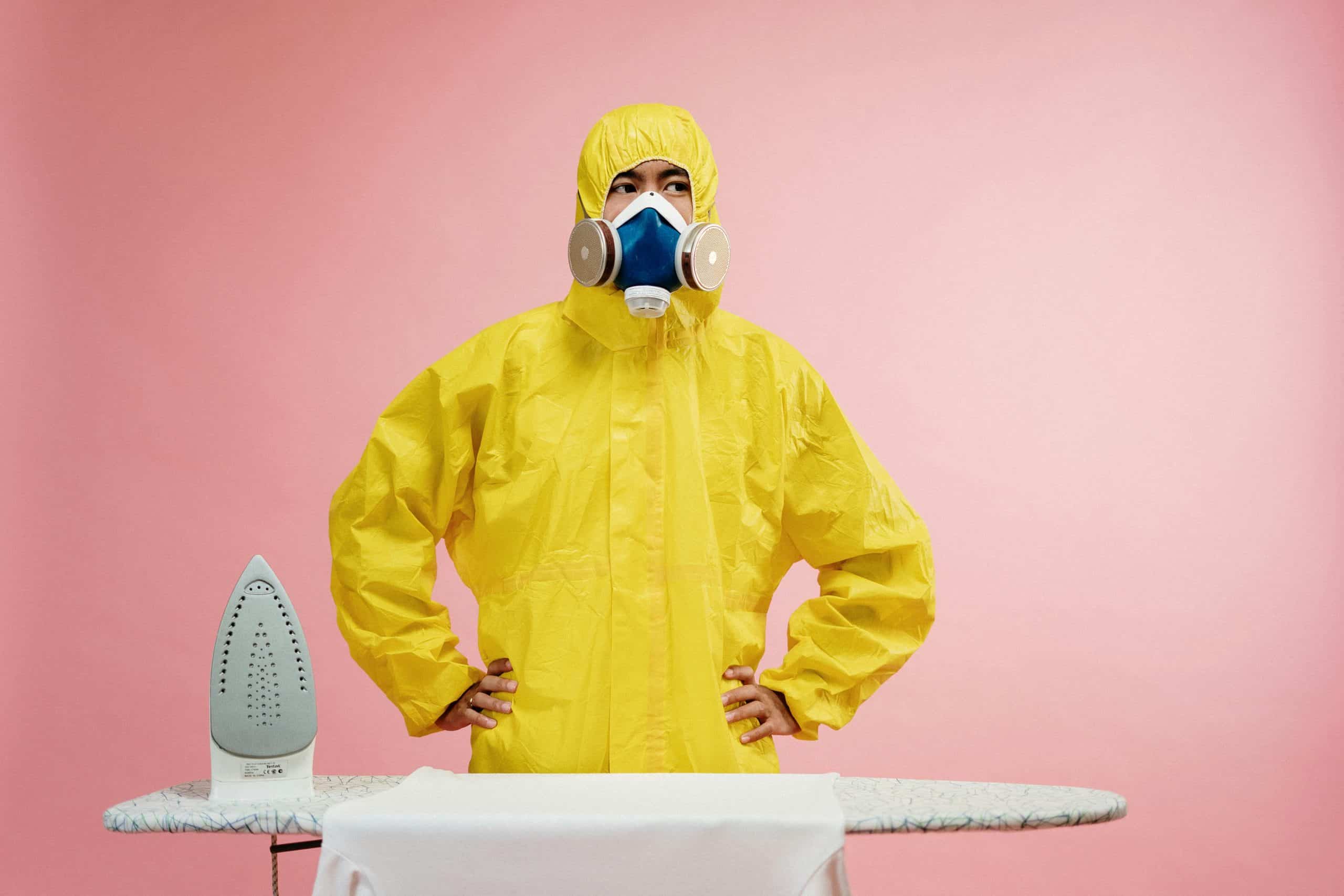 Humorous scene of a man in a yellow hazmat suit ironing during quarantine.