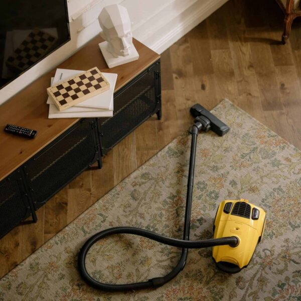 Fall deep cleaning. Warm living room scene featuring a yellow vacuum on a floral carpet with a vintage vibe.