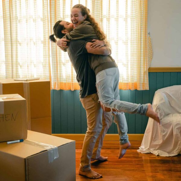 This photograph features a happy couple in an apartment with boxes. Micro-ceremonies can help create positive experiences for people living together.