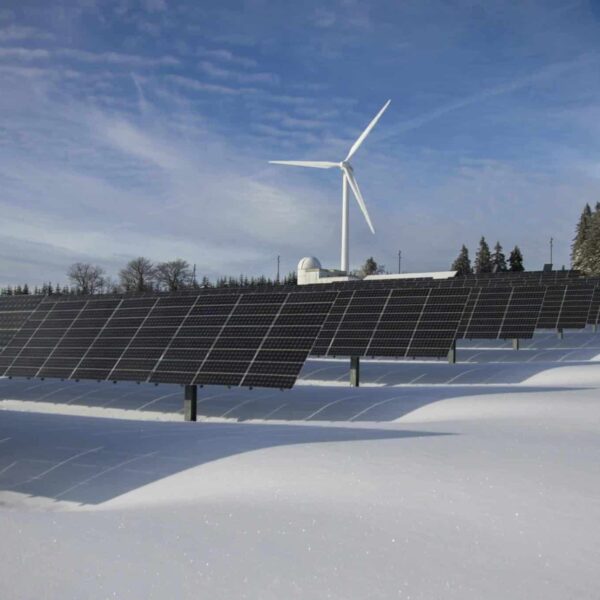 Solar panels and a wind turbine in a snowy landscape, illustrating renewable energy sources supported by Solar Tax Credits.