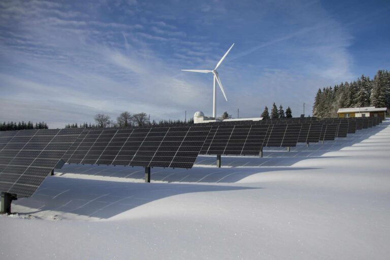 Solar panels and a wind turbine in a snowy landscape, illustrating renewable energy sources supported by Solar Tax Credits.