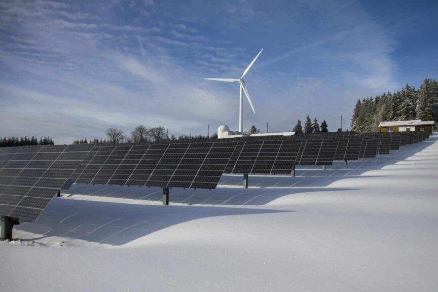 Solar panels and a wind turbine in a snowy landscape, illustrating renewable energy sources supported by Solar Tax Credits.