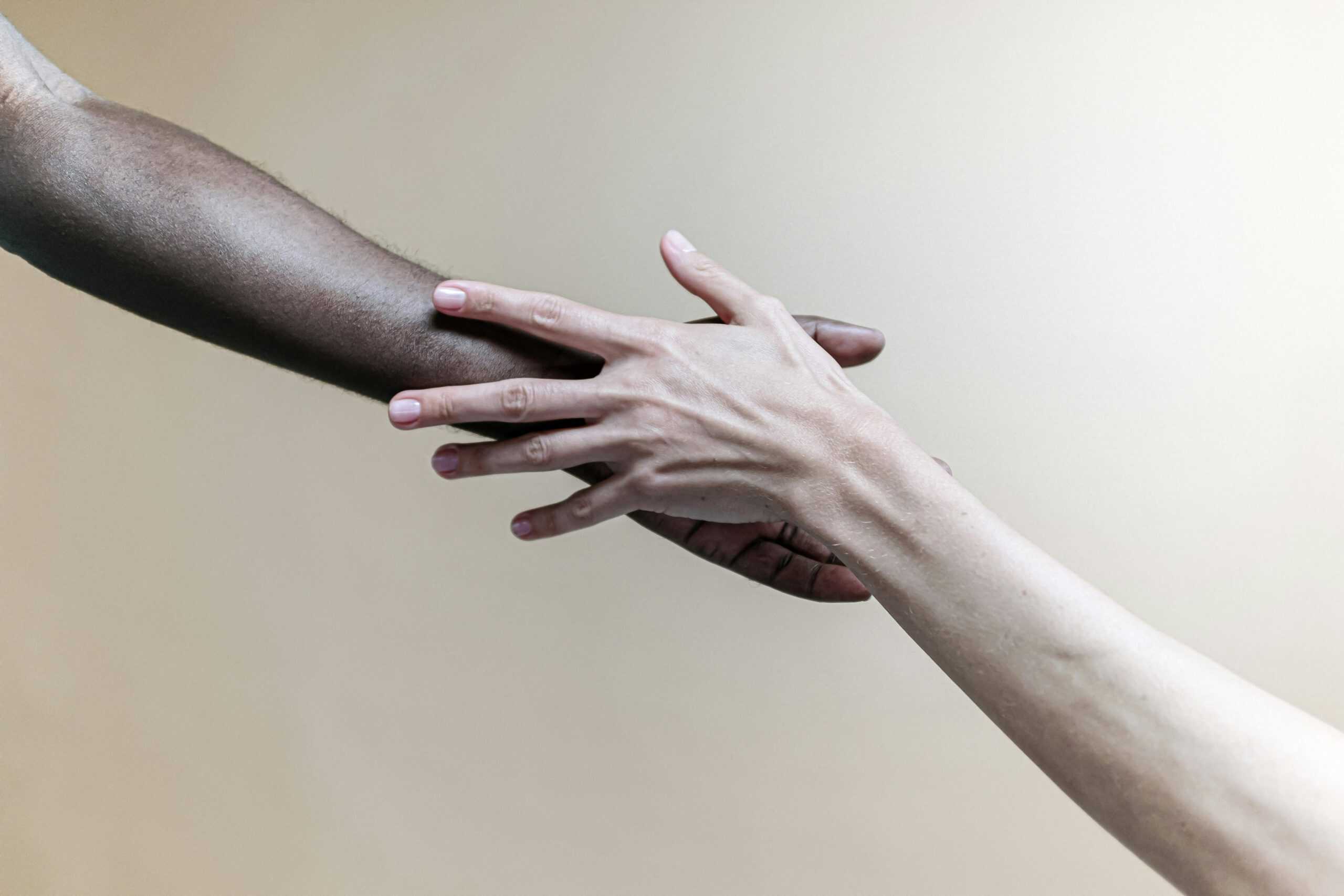 Two hands of different ethnicities reaching out, symbolizing diversity and connection.