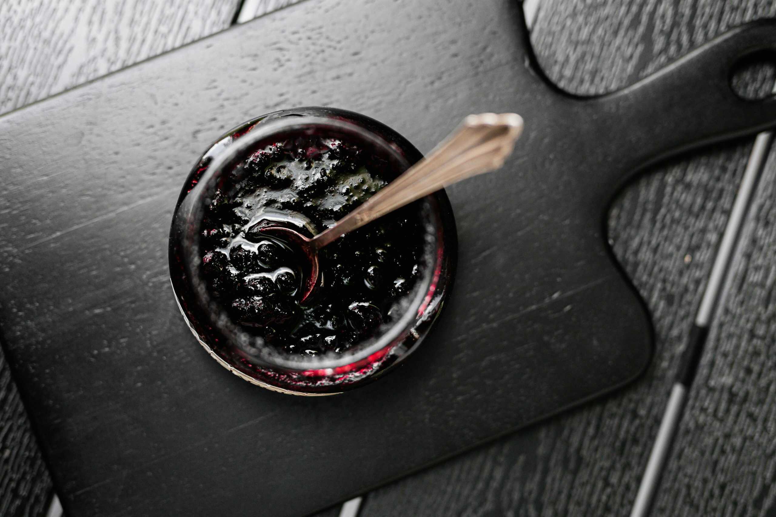 Aerial shot of a jar of dark jam on a wooden board with a spoon, perfect for food photography.