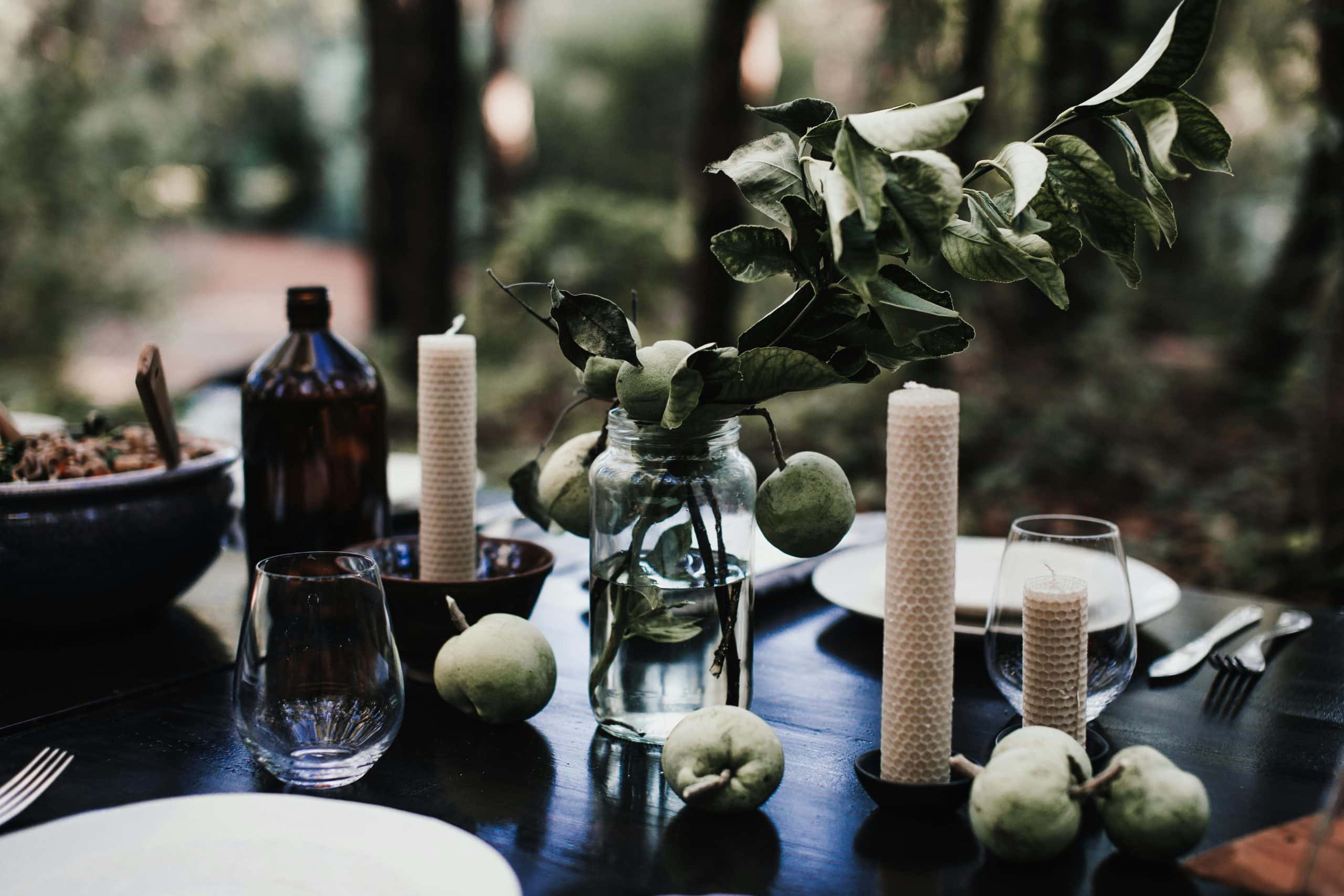 diy, autumn, A rustic table setting outdoors with candles, green apples, and leafy branches creating a serene ambiance.
