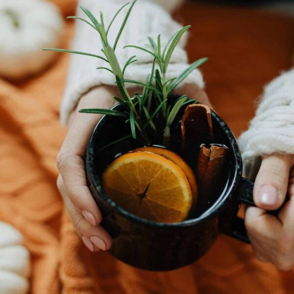 pumpkin spice, Hands holding a warm cup with spices and orange slices, surrounded by autumn decorations.