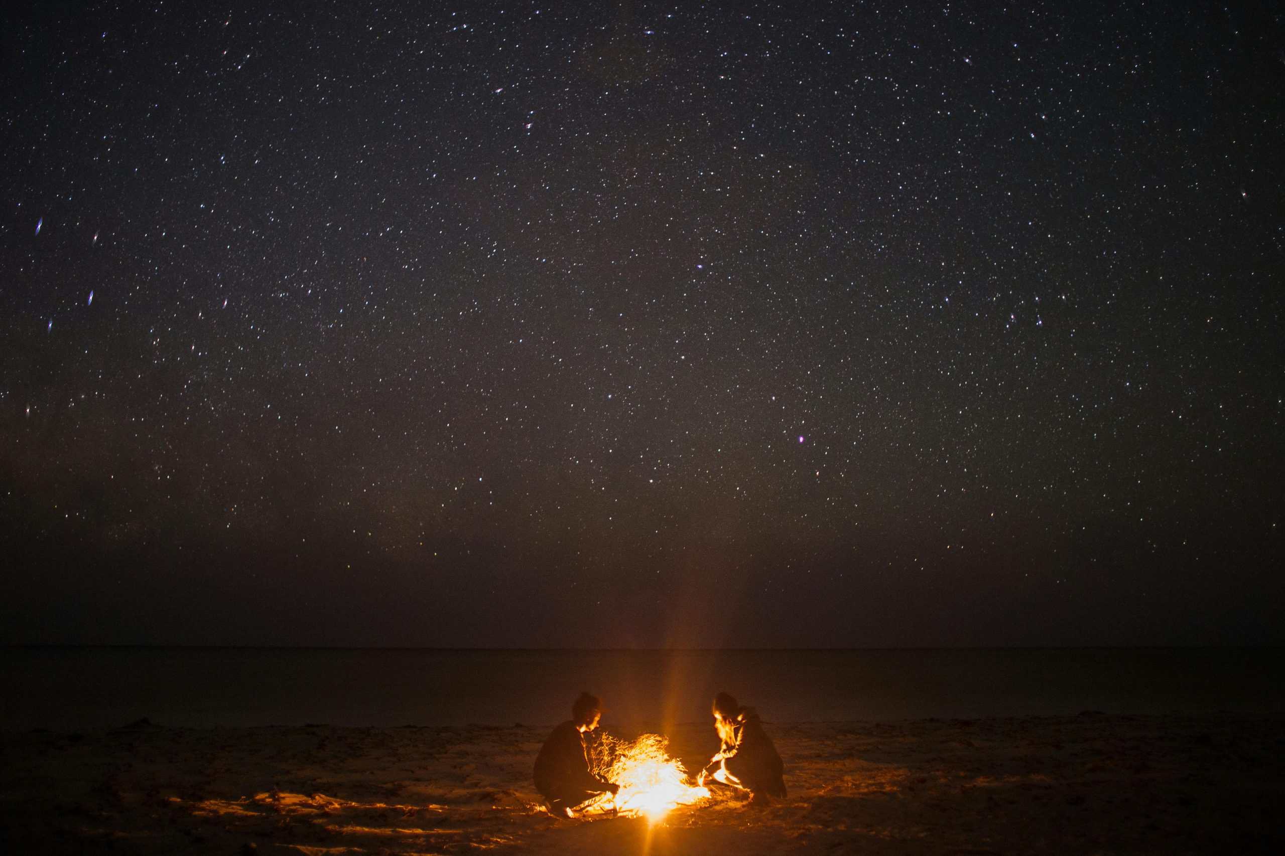 A couple enjoying a bonfire on a serene beach under a starlit sky, perfect for night photography themes.