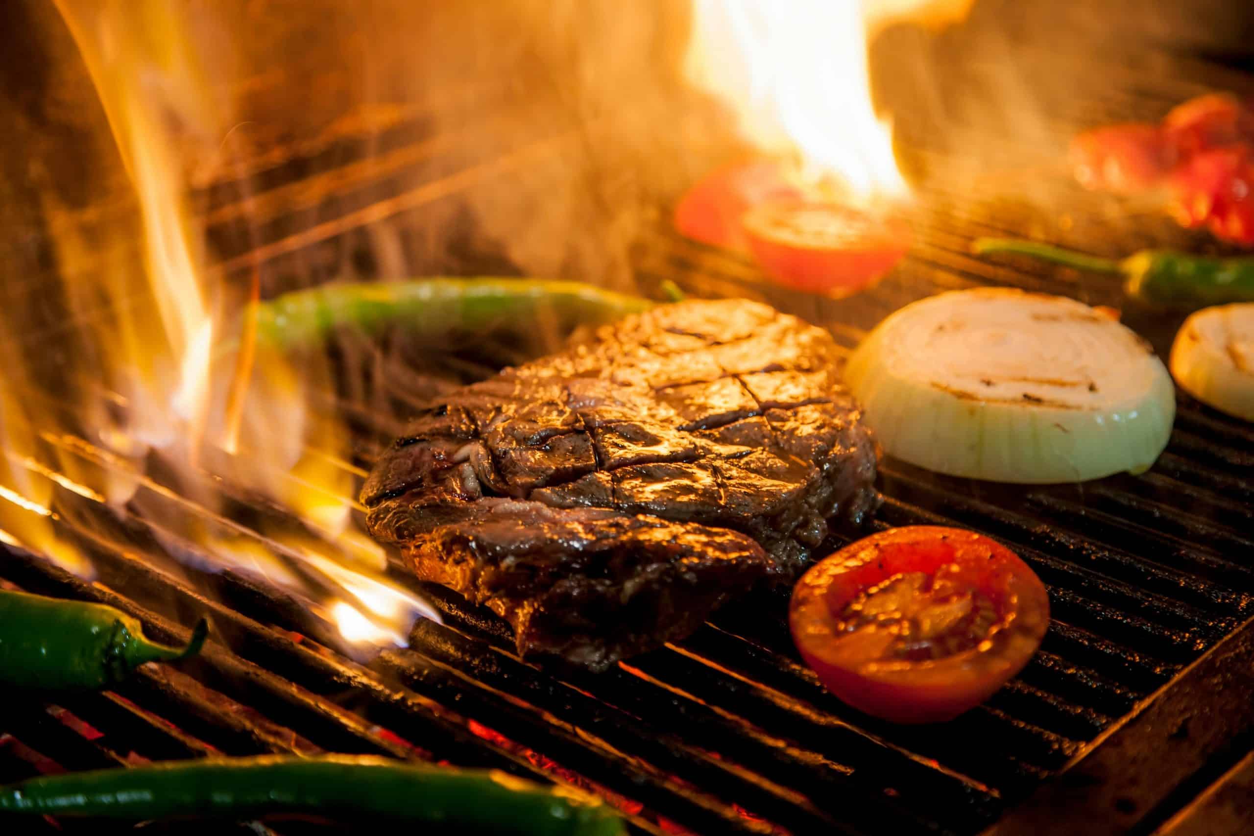 Flame-grilled steak with onions and tomatoes on a barbecue grill, ready to savor.
