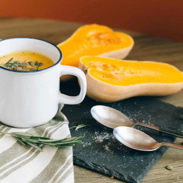 A cozy setting with butternut squash soup in a mug, complemented by fresh ingredients and rustic decor. pumpkin