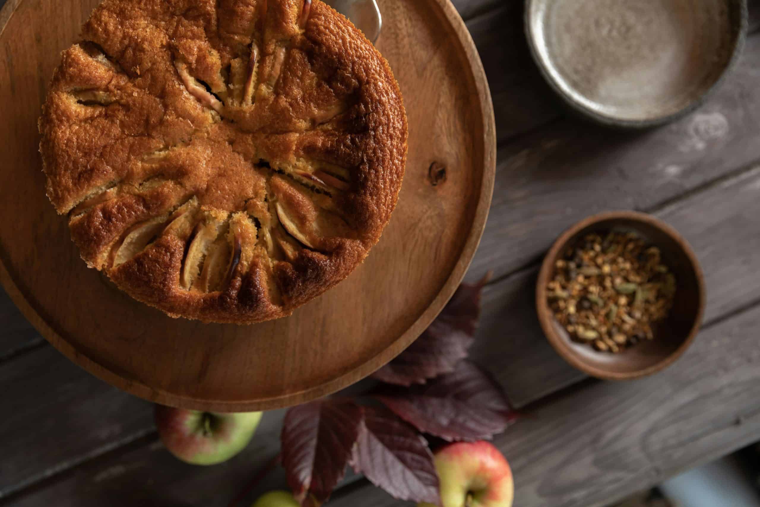 A delicious rustic apple cake on a wooden table with apples and spices.