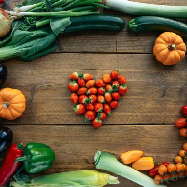 in-season, Vibrant fruits and vegetables arranged heart-shaped on a wooden surface, top view.