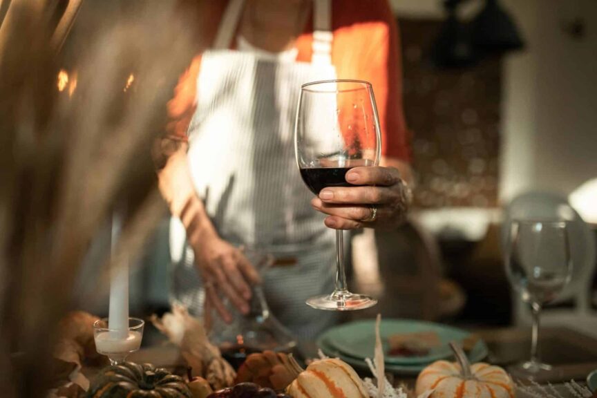 Cozy indoor autumn dinner setting with a person holding a glass of red wine, surrounded by festive decor. fall, wine, wine season, fall wine season traveling