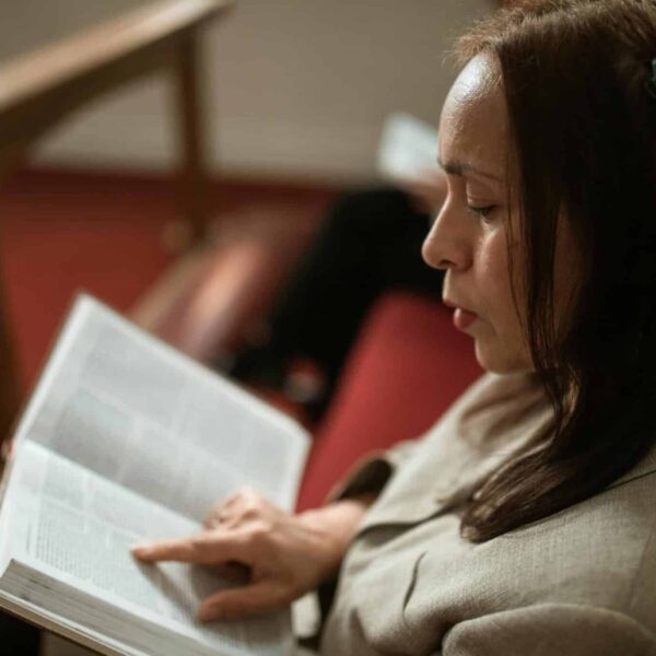 A woman in a church pew reading a Bible, showing devotion and faith, women, lessons