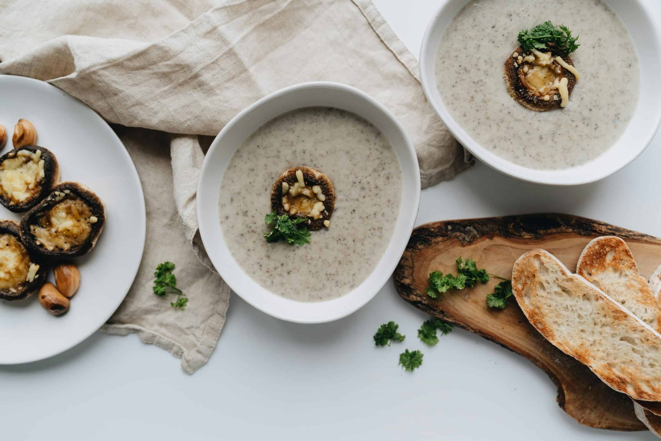 A flat lay of mushroom soup, stuffed mushrooms, and bread on a wooden board.