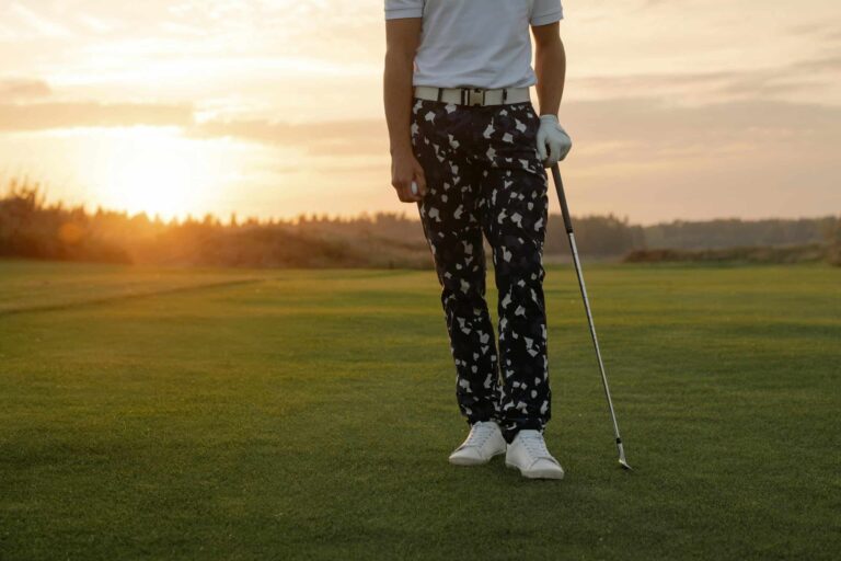Golfer holding a club on a scenic golf course at sunset, exuding professionalism.