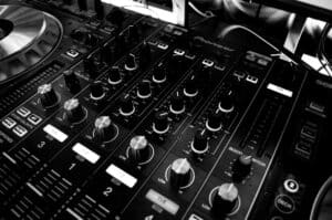 Black and white close-up of a DJ's audio mixing console with knobs and controls. Omen
